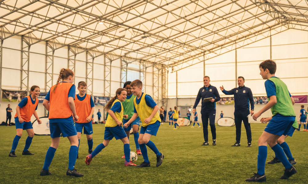 Inspiring photograph of diverse youth soccer players aged 8-16 training on indoor green turf field, professional coaches guiding drills, warm golden lighting from above, sense of community and inclusion, premium sports photography style
